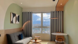 Una sala de estar moderna con un sofá, dos mesas auxiliares, una mesa de comedor y un amplio ventanal con cortinas.