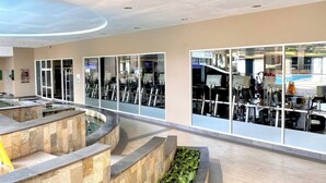 Un gimnasio moderno con equipo de ejercicio, un elemento decorativo de agua y suelo de baldosas de piedra.