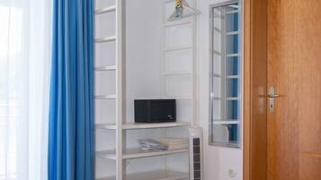 Une chambre à coucher avec un lit, une étagère blanche, un miroir et une porte.
