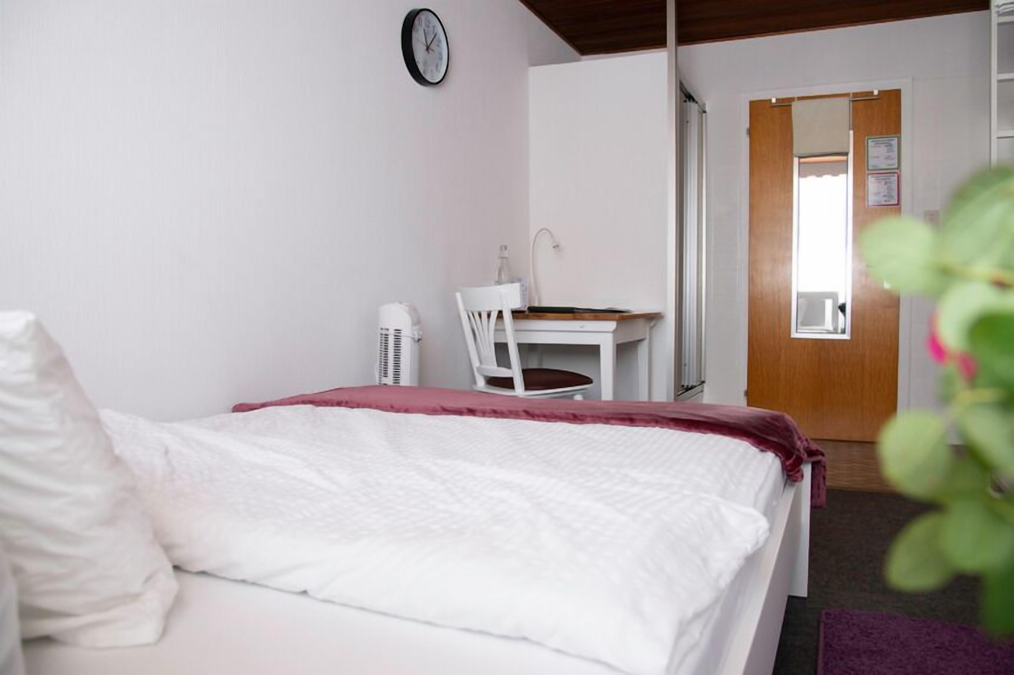 Une chambre à coucher avec un lit, un bureau, une chaise, une horloge et une porte.