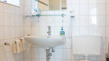 A bathroom with white tiles, a sink, a toilet, a trash bin, and a mirror.