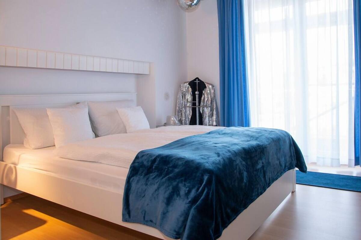 A neatly made bed with a dark blue bedspread, white pillows, and a white headboard.