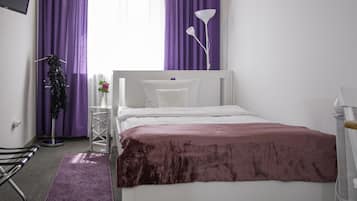 Quarto com cama branca, cortinas roxas, abajur branco e tapete roxo.