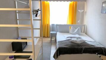 Une chambre d’hôtel comprenant un lit, un bureau, une chaise, une étagère et une fenêtre avec des rideaux.