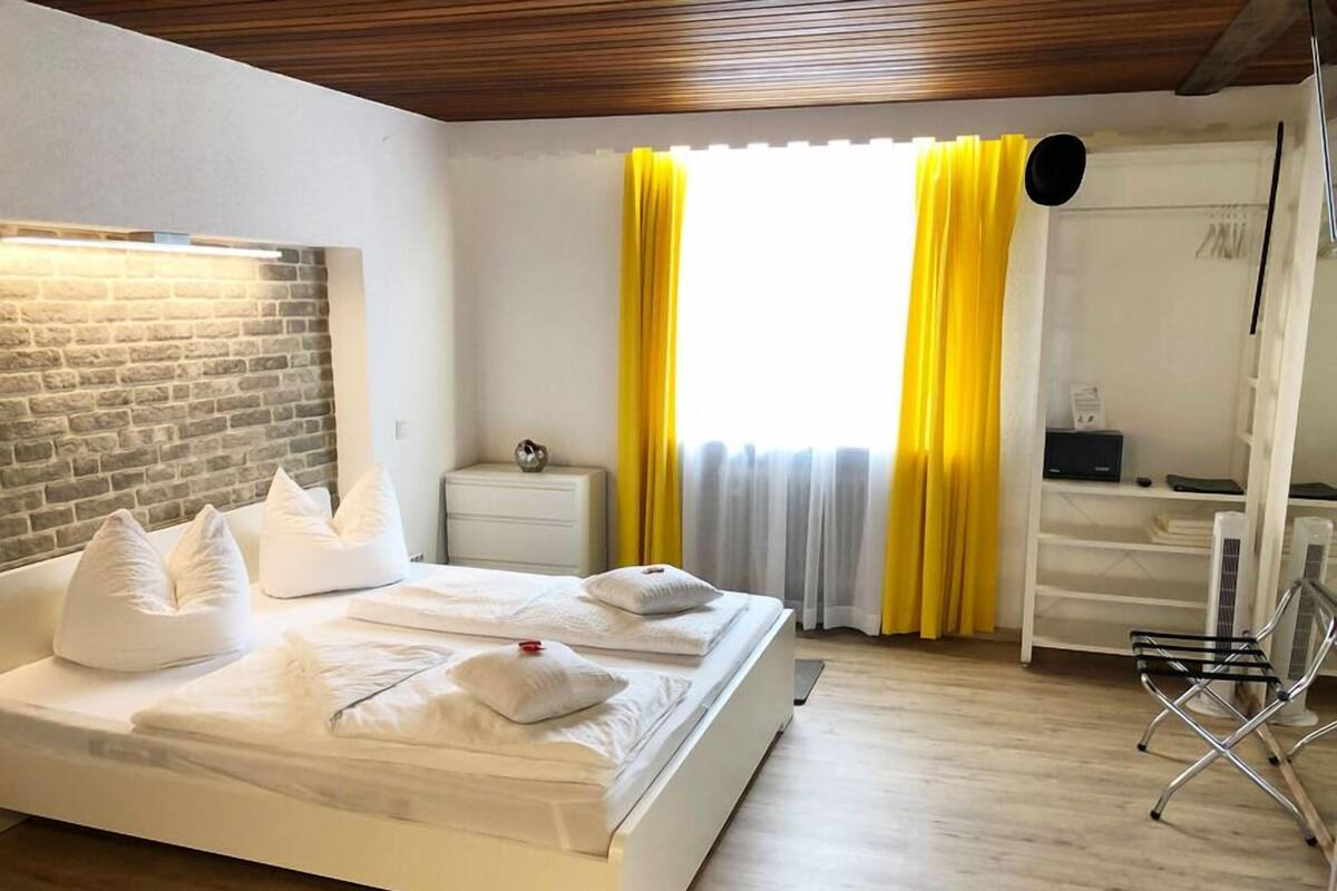 A hotel room with a bed, a nightstand, a chair, and a desk with a computer.