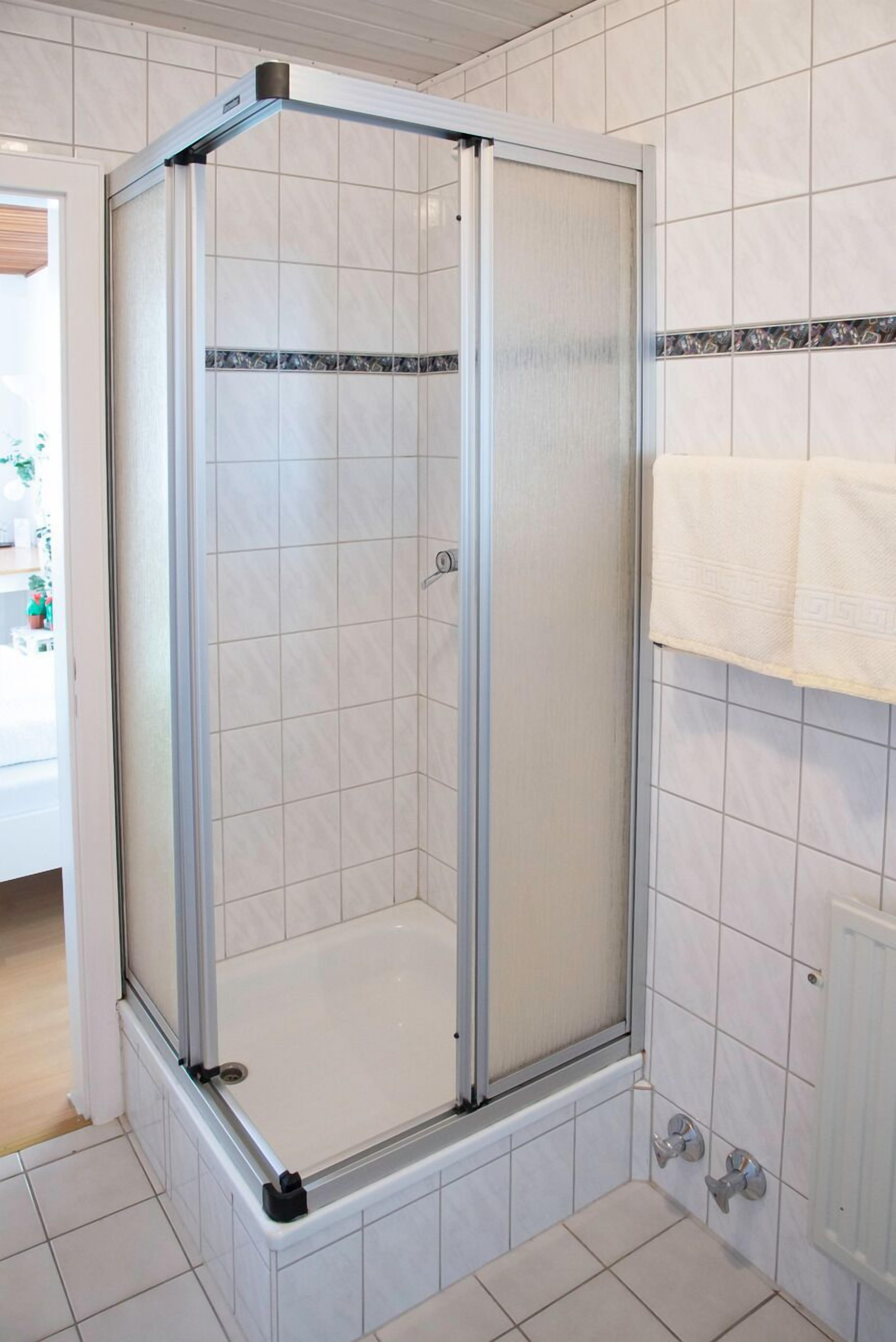 Un espace de douche doté d’une porte en verre, de murs recouverts de carreaux blancs et d’un porte-serviettes avec deux serviettes.