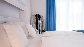 A hotel room with a bed, white bedding, a hanging coat rack, and a window with blue curtains.