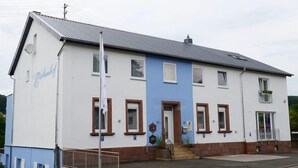 A two-story building with a white and blue facade, a grey roof, and a small porch area with steps leading to the entrance. - Birkenhof Family Lodge  (Rieschweiler-Mühlbach)