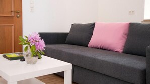 A grey sofa with a pink pillow, a white coffee table, and a vase with flowers. - Birkenhof Family Lodge  (Rieschweiler-Mühlbach)