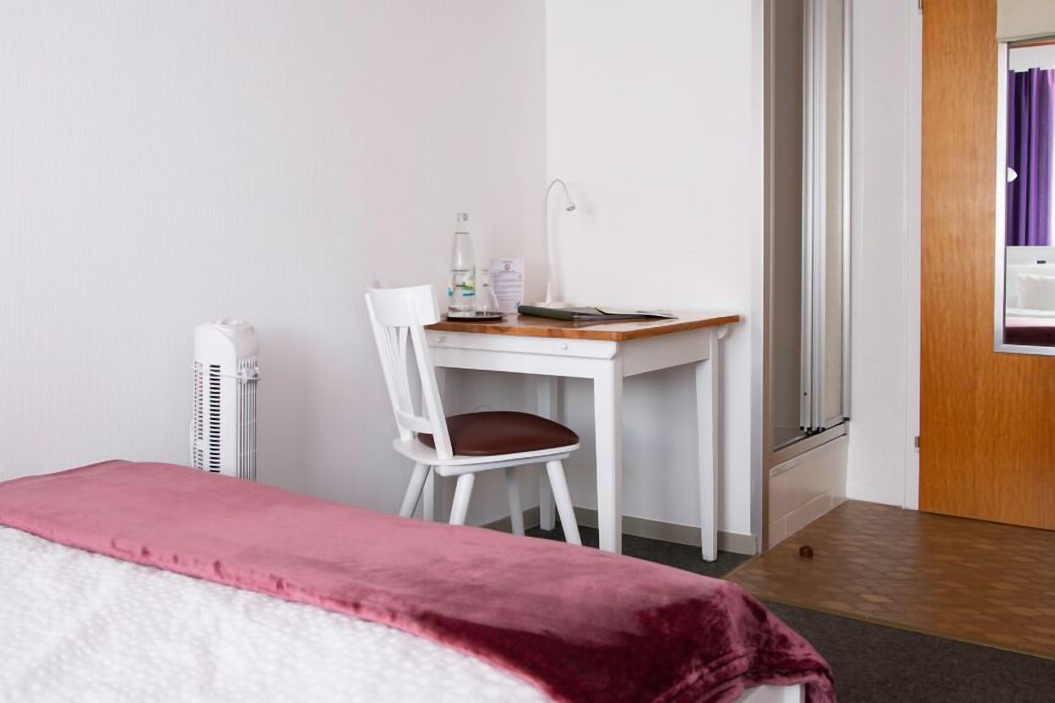 Une chambre d’hôtel comprenant un lit, un bureau avec une chaise, un radiateur et une porte donnant accès à une salle de bain.