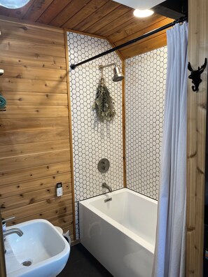 A bathroom with a wooden wall, a hexagonal patterned wall, a bathtub, a sink, a shower curtain, and a wall-mounted towel rack.