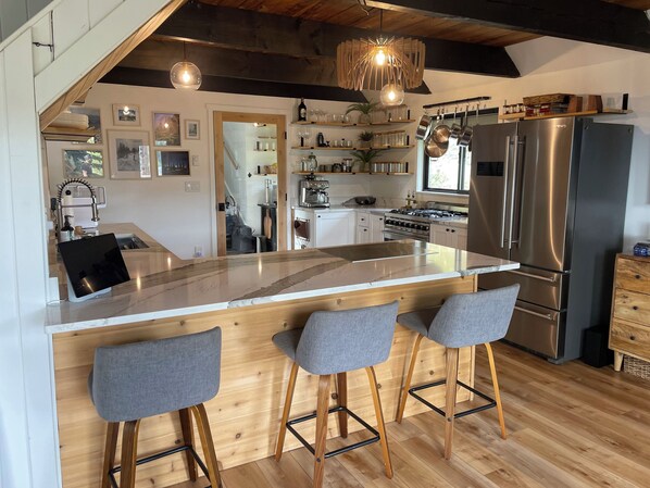 A modern kitchen with a large island, bar stools, stainless steel appliances, and wooden accents.