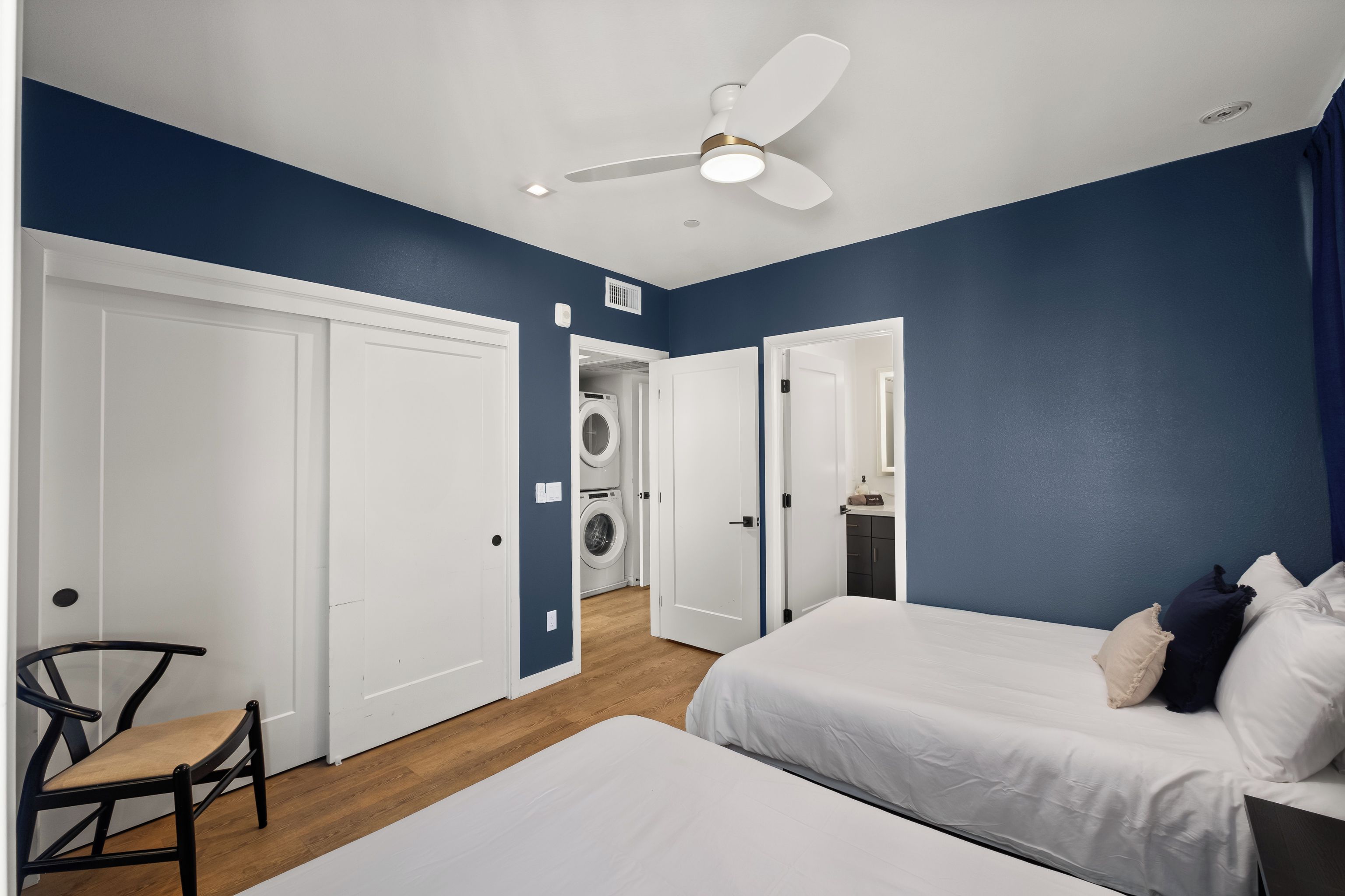 A hotel room with two beds, a ceiling fan, a washing machine, and a chair.