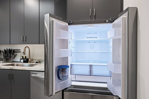 An open refrigerator with a water dispenser and a blue jug inside. - King Bed, EV Charger, Sleeps 8, Balcony, Laundry (San Diego)
