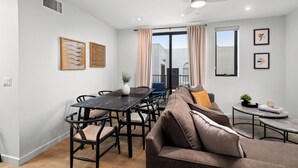 Ein modernes Wohnzimmer mit einer Couch, einem Esstisch und Stühlen. Es gibt einen Deckenventilator, ein Fenster mit Vorhängen und Kunstwerke an den Wänden.