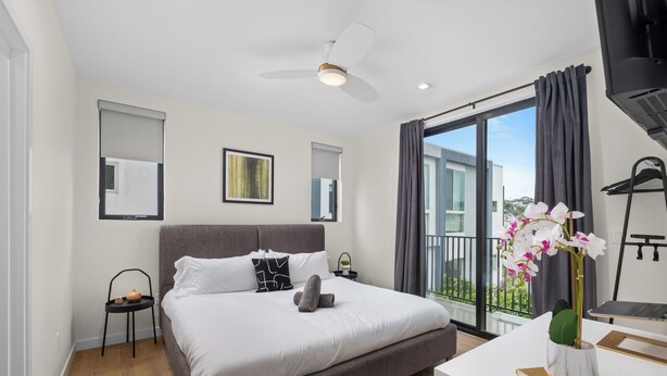 Ein modernes Hotelzimmer mit einem großen Bett, einem Schreibtisch mit Laptop, einem Deckenventilator und einem Balkon mit Blick.