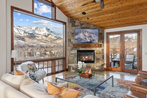 A spacious living room with a fireplace, large windows offering mountain views, and a cozy seating area. - New! Stunning Mountain Views, Private Hot Tub, Perfect Layout (Mountain Village)