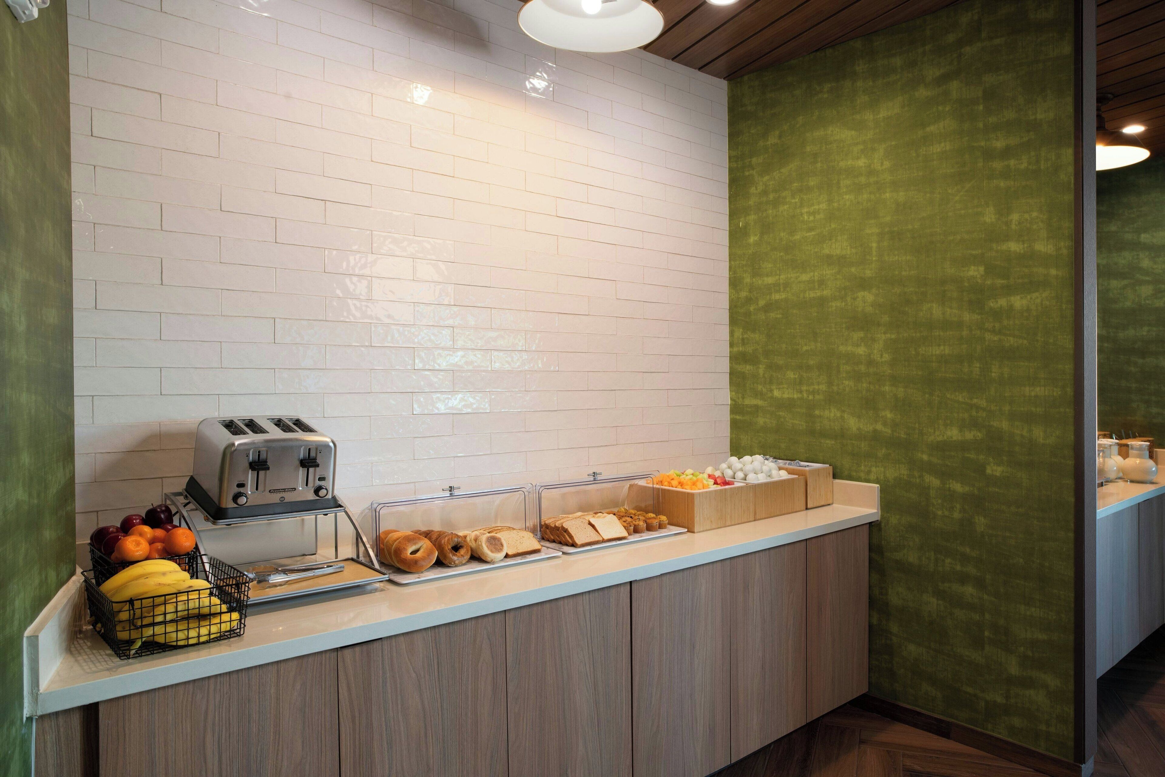 A breakfast bar with a toaster, fruits, and pastries.
