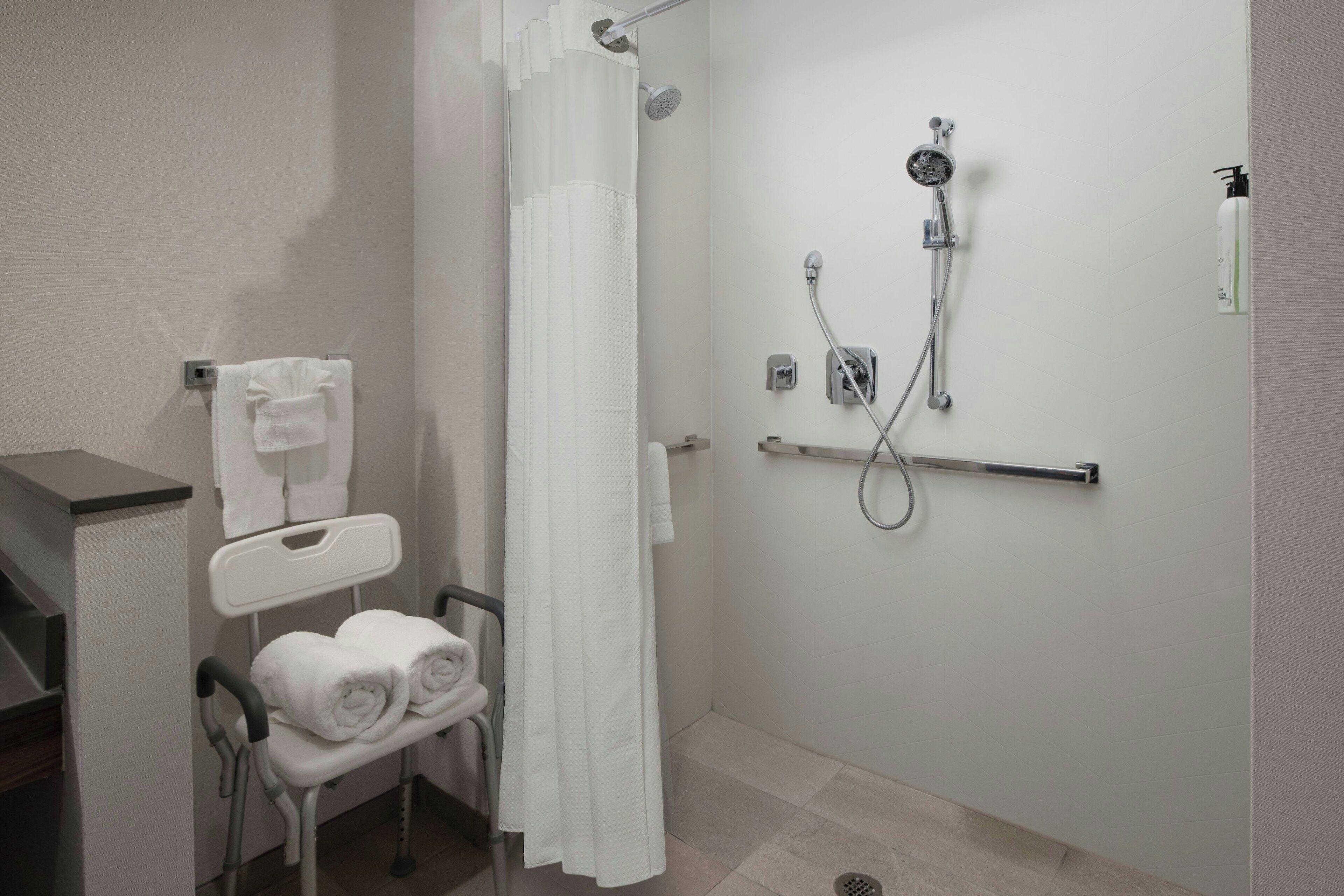 A modern bathroom with a shower, a wheelchair-accessible bench with towels, and a hand dryer.