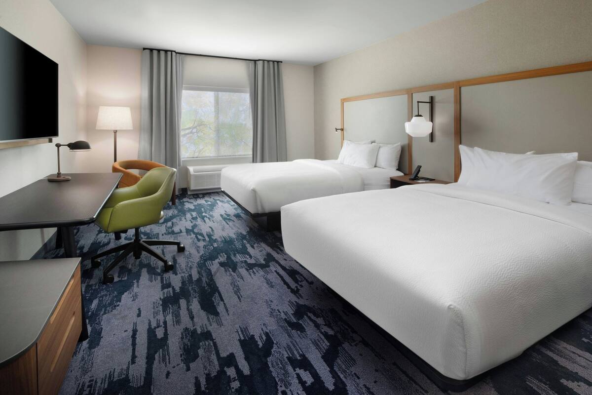A hotel room with two beds, a desk, a chair, a TV, and a window with curtains.