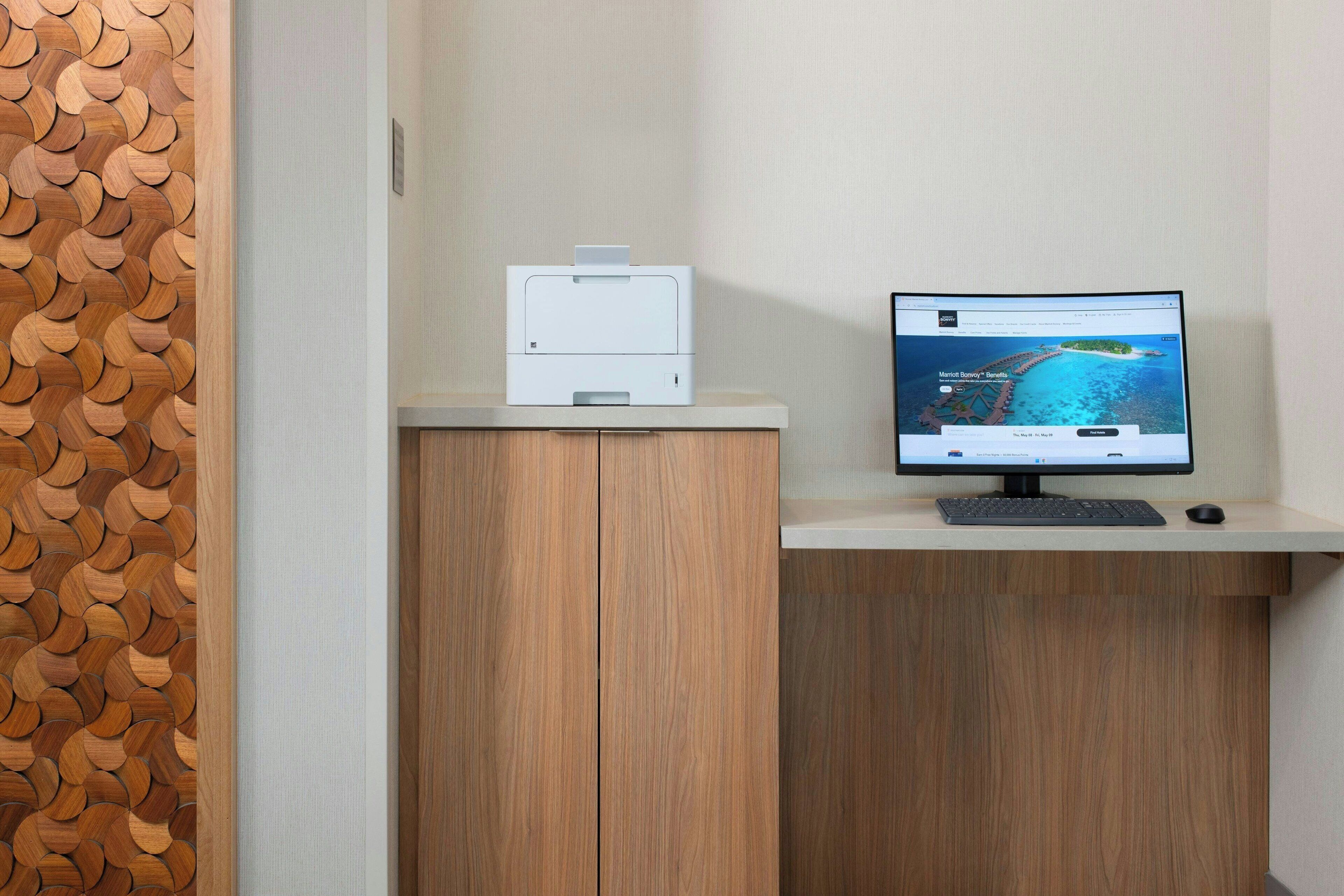 A computer desk with a printer and a monitor displaying a travel website.