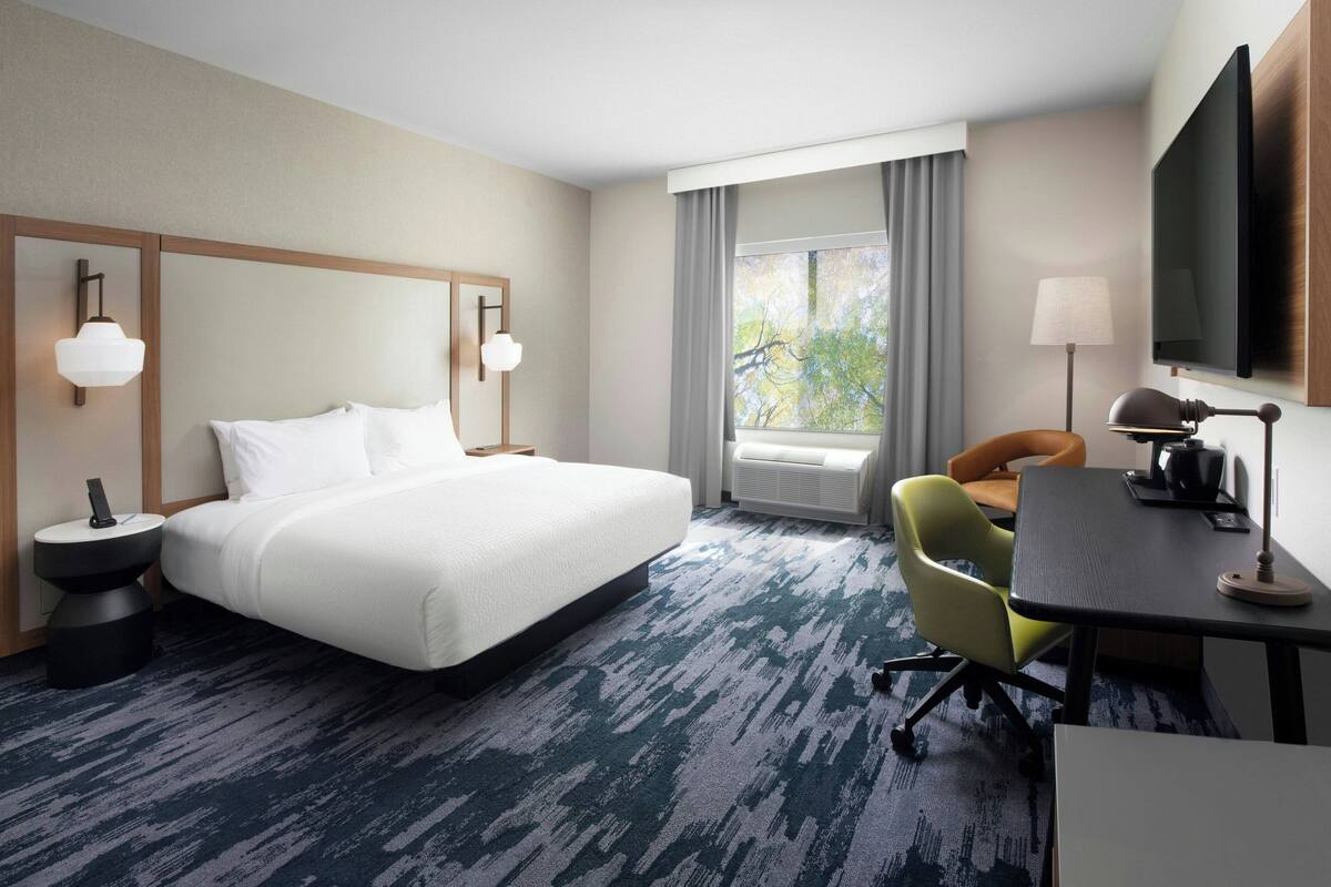 A hotel room with a large bed, a desk with a chair, a television, and a window with curtains.