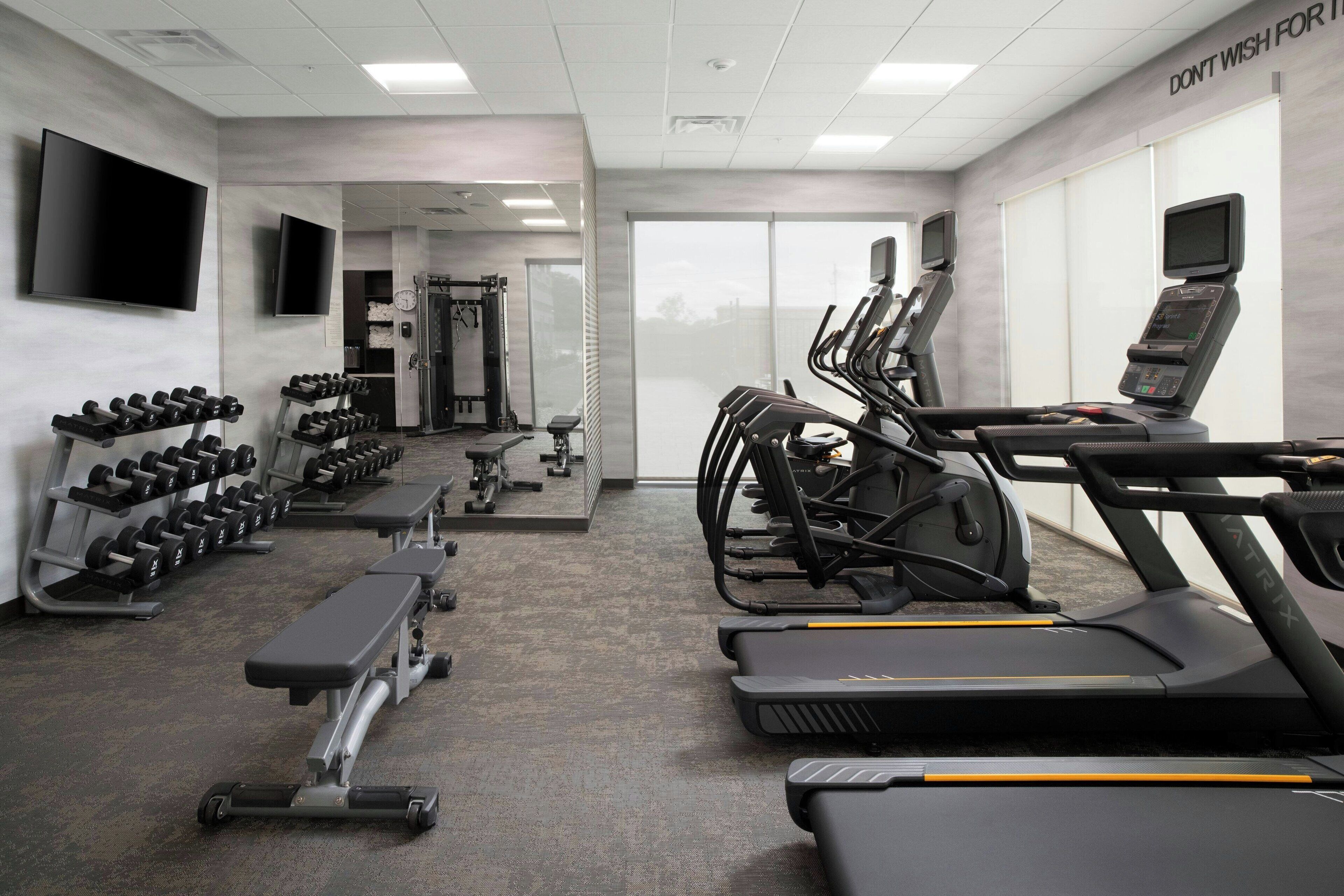 Une salle de sport équipée de tapis de course, d’haltères et de bancs.