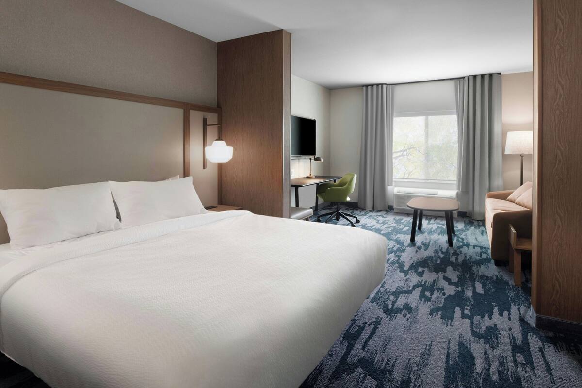 A hotel room with a large bed, a desk, a chair, and a sofa.