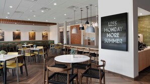 A modern restaurant with a herringbone floor pattern, round tables, and black wicker chairs.