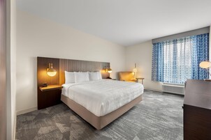Una habitación de hotel con una cama grande, lámparas de noche, una silla, un escritorio y una ventana con cortinas.