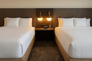 Une chambre d’hôtel avec deux lits, une table de chevet et deux lampes fixées au mur.