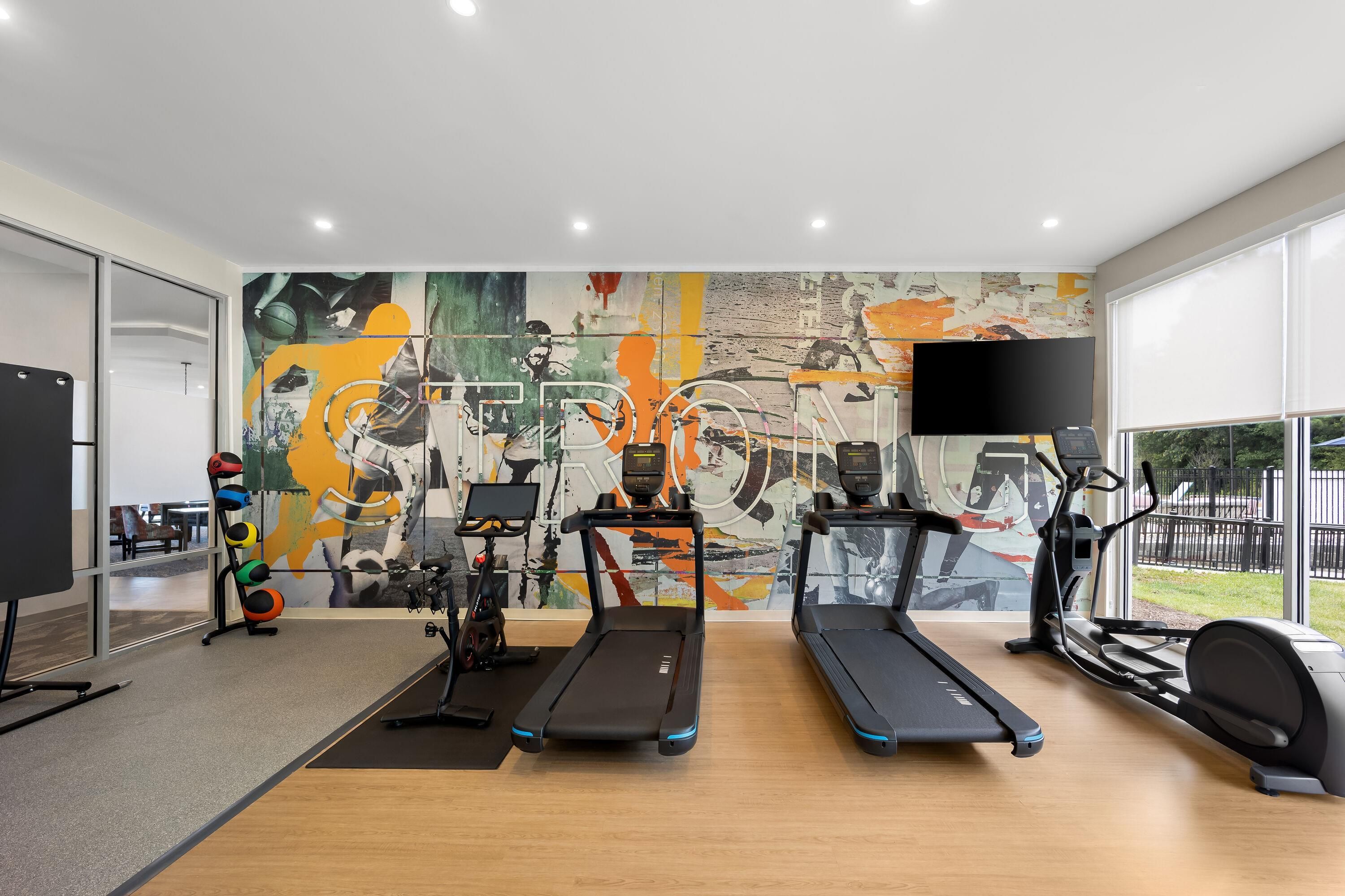 A modern gym with exercise equipment, a large abstract mural, and a large TV screen.