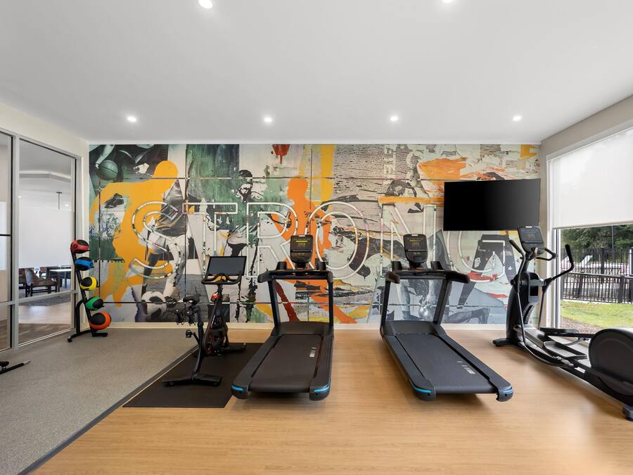 A modern gym with exercise equipment, a large abstract mural, and a large TV screen.