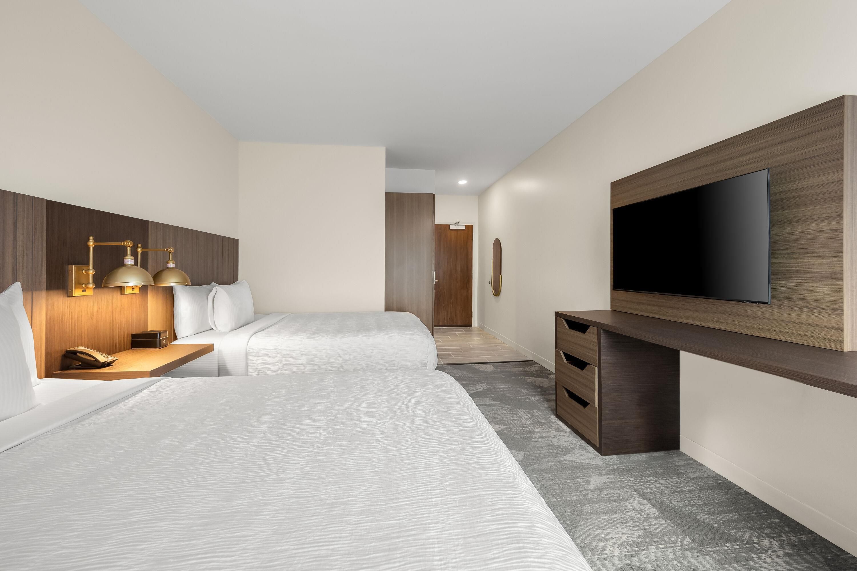 Habitación de hotel con dos camas, un escritorio con teléfono, un televisor de pantalla plana y un armario de madera.