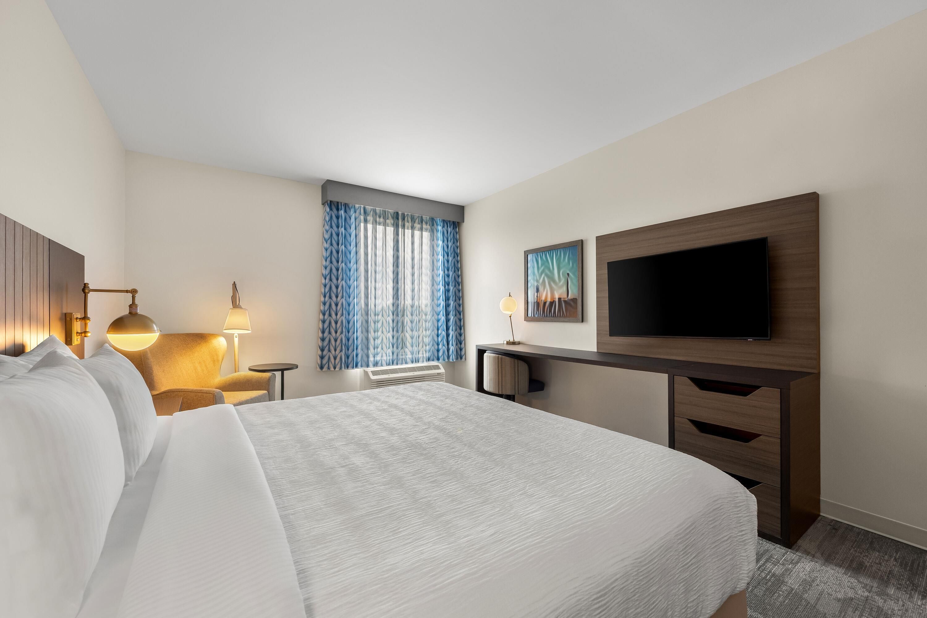 A hotel room with a bed, a desk, a television, and a window with curtains.