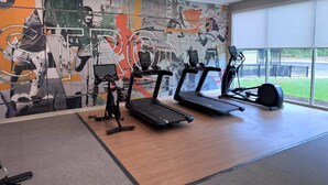 Un gimnasio con cintas de correr, elípticas y un gran mural en la pared.