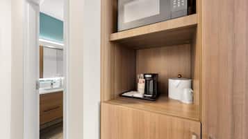 A hotel room with a built-in microwave on a wooden shelf, a coffee maker, and a tissue box.