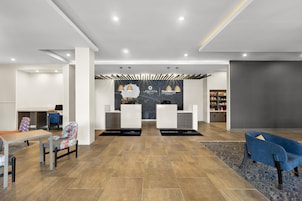 Un área de recepción moderna con mostrador, dos sillas, una máquina de café y una zona de estar con mesa y sillas.