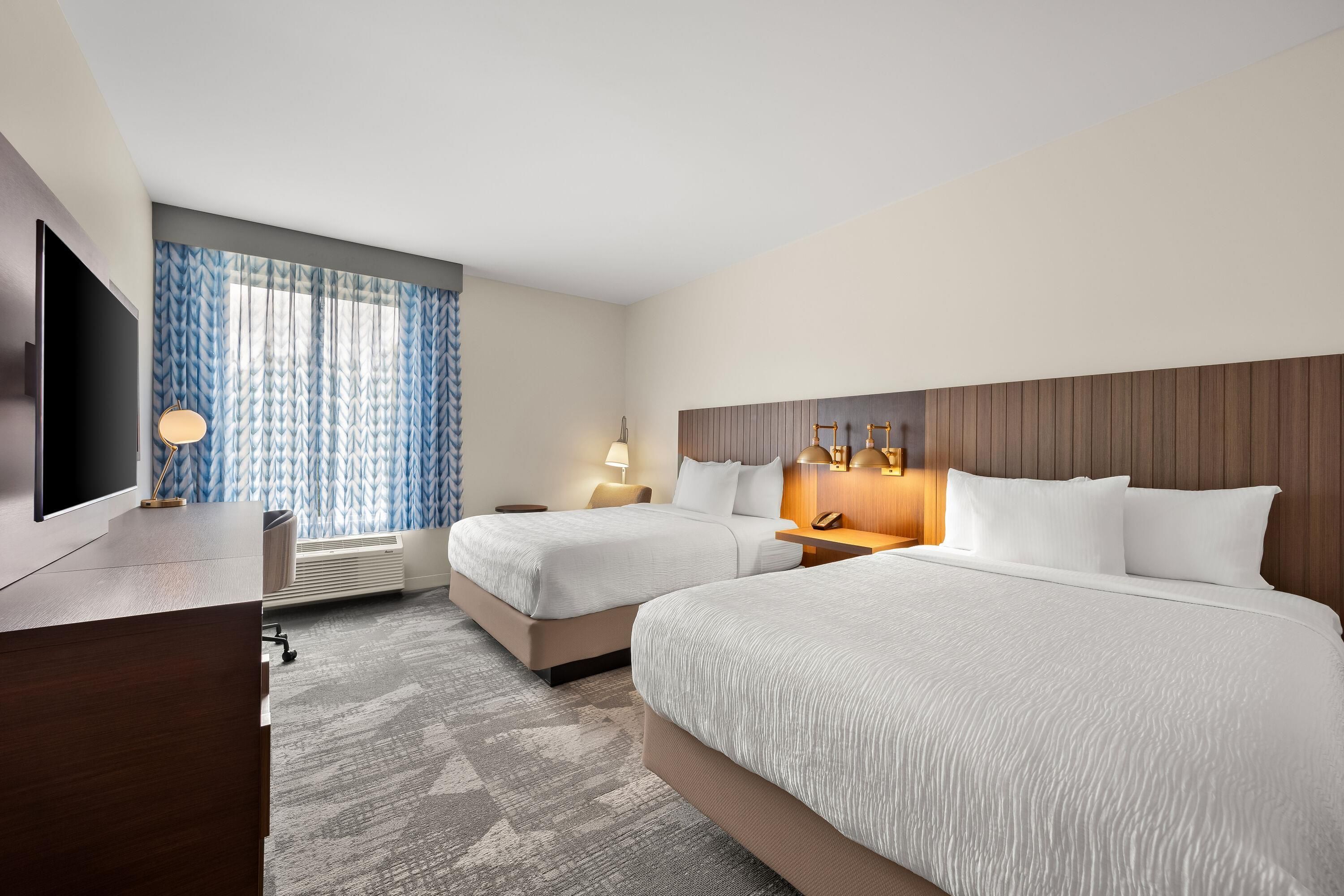Habitación de hotel con dos camas, un escritorio, un televisor y una ventana con cortinas.