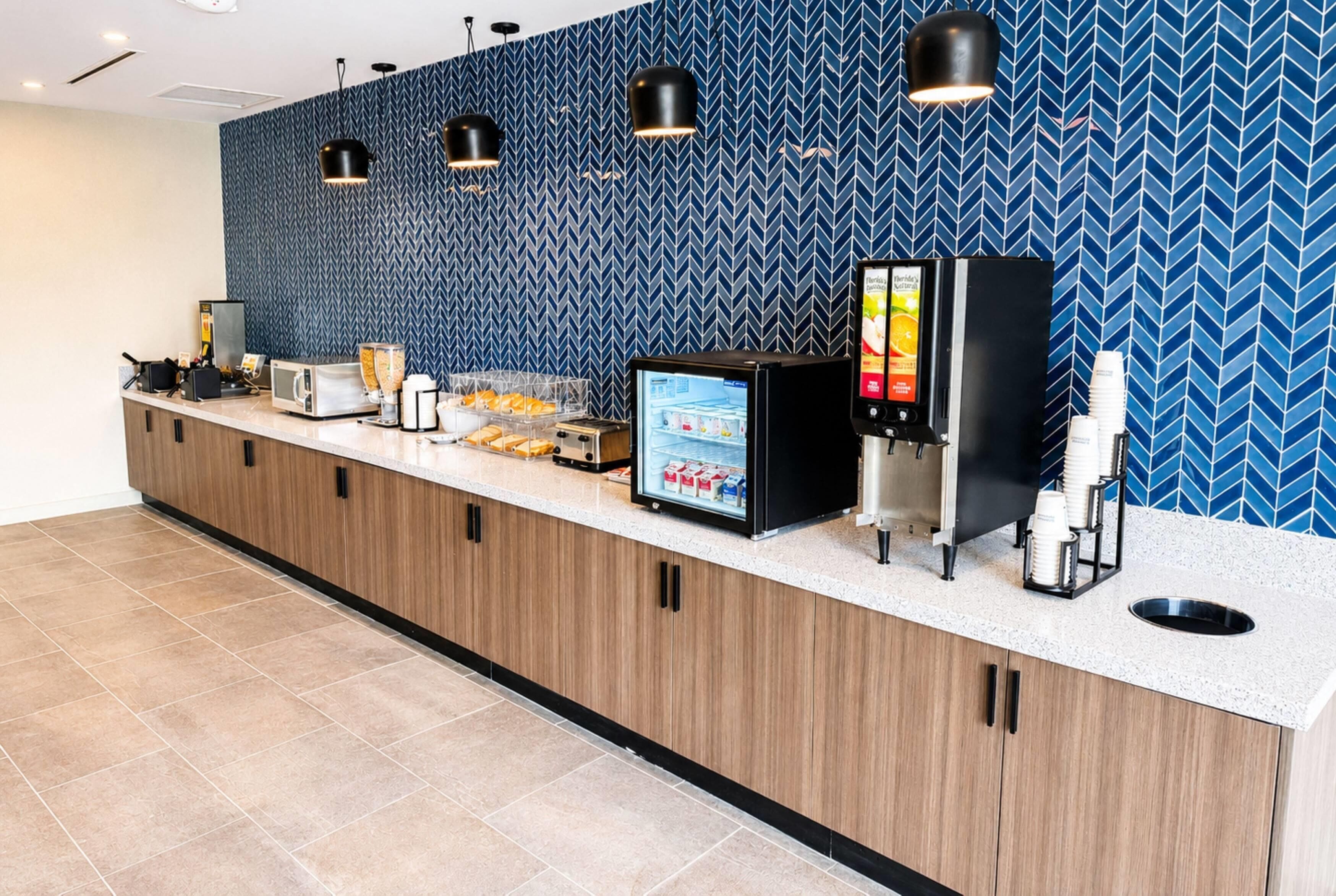 A hotel reception area with a counter, a digital menu display, a coffee machine, and a refrigerator.