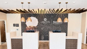 Un mostrador de recepción con dos mostradores, una pared con mapa, luces colgantes y un techo de listones de madera.