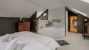 A modern bedroom with a large bed, a freestanding bathtub, and a vanity with a mirror. - Stone Cottage Norfolk , Lovely Family Cottage (Norwich)