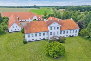 A large, white building with a red-tiled roof, surrounded by well-maintained lawns and trees. - Hindemae Estate An Exclusive Experienc (Ullerslev)
