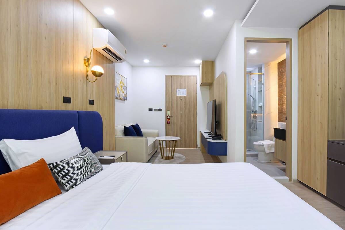 Ein modernes Hotelzimmer mit einem großen Bett, einem kleinen Schreibtisch, einem Fernseher und einem durchgegangene Tür erkennbaren Badezimmer.