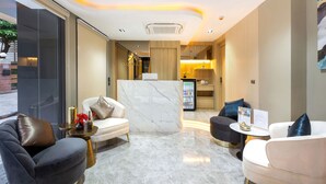 Un hall d’hôtel moderne avec un sol en marbre, un comptoir d’accueil et des espaces détente dotés de fauteuils en cuir et en tissu.