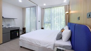 Une chambre d’hôtel moderne dotée d’un grand lit, d’un bureau avec un réfrigérateur et offrant une vue sur la verdure par les fenêtres.
