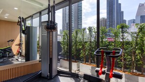 Une salle de sport moderne, équipée de machines d’exercice, dotée de grandes fenêtres et offrant une vue sur les bâtiments de la ville.