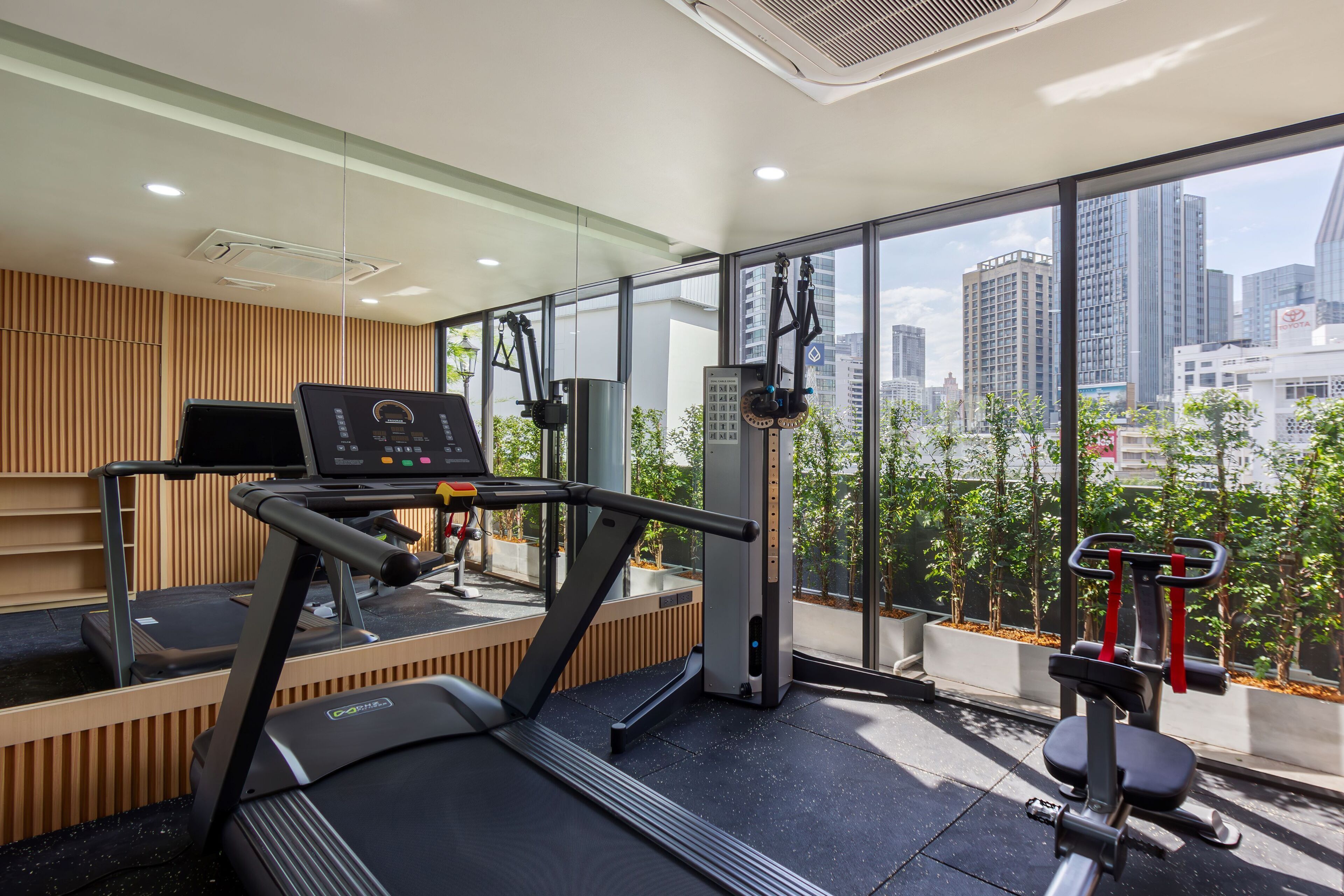 Une salle de sport moderne équipée d’un tapis de course, d’un vélo elliptique et d’appareils de musculation, avec de grandes fenêtres offrant une vue sur la ville.