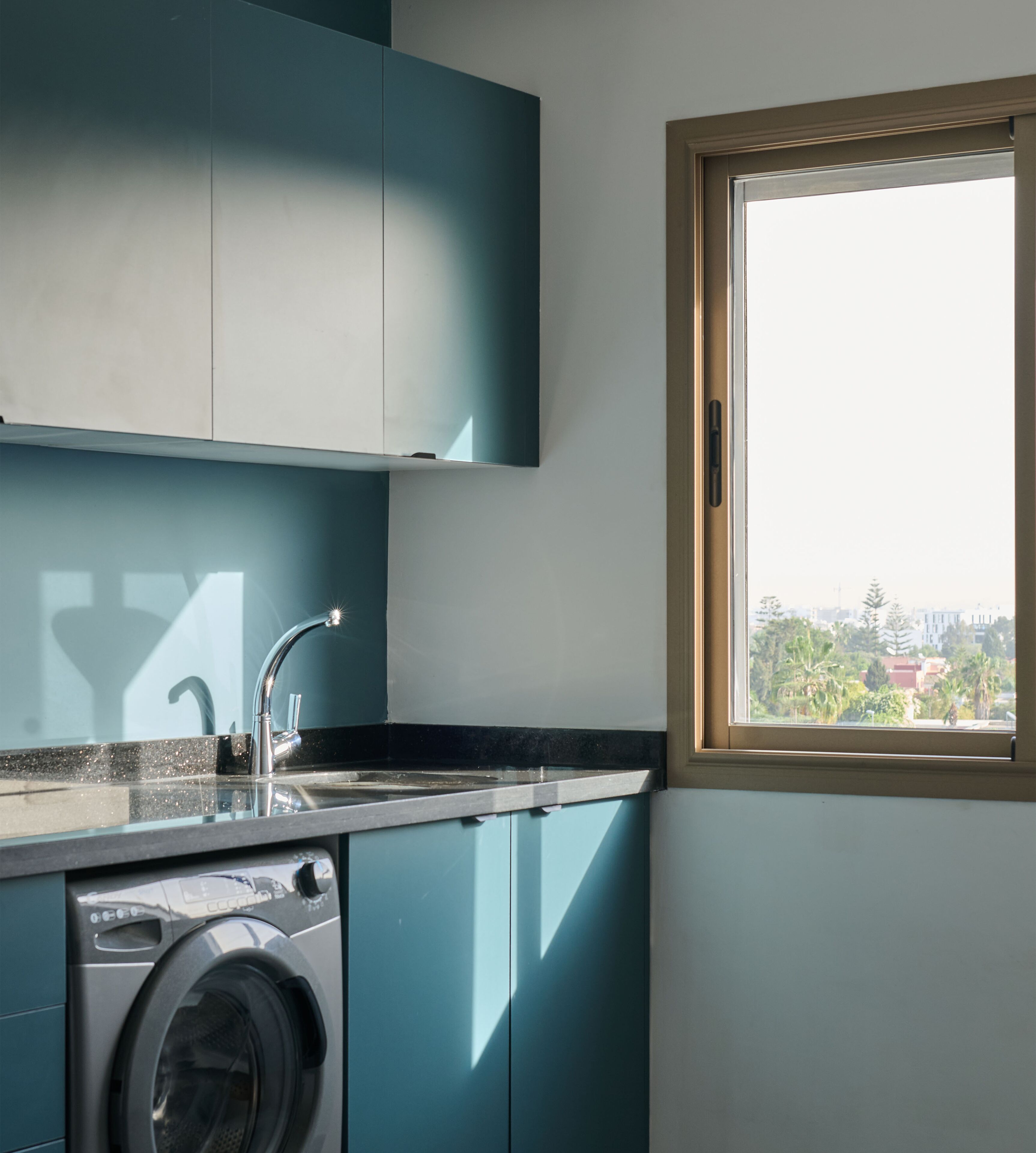 Cocina compacta con lavadora, lavaplatos y ventana con vista a edificios.