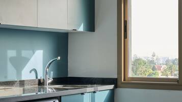 Une cuisine compacte équipée d’un lave-linge, d’un évier et d’une fenêtre donnant sur des immeubles.